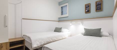 A bedroom with two beds, a wooden shelf, a window, and two framed pictures on the wall.