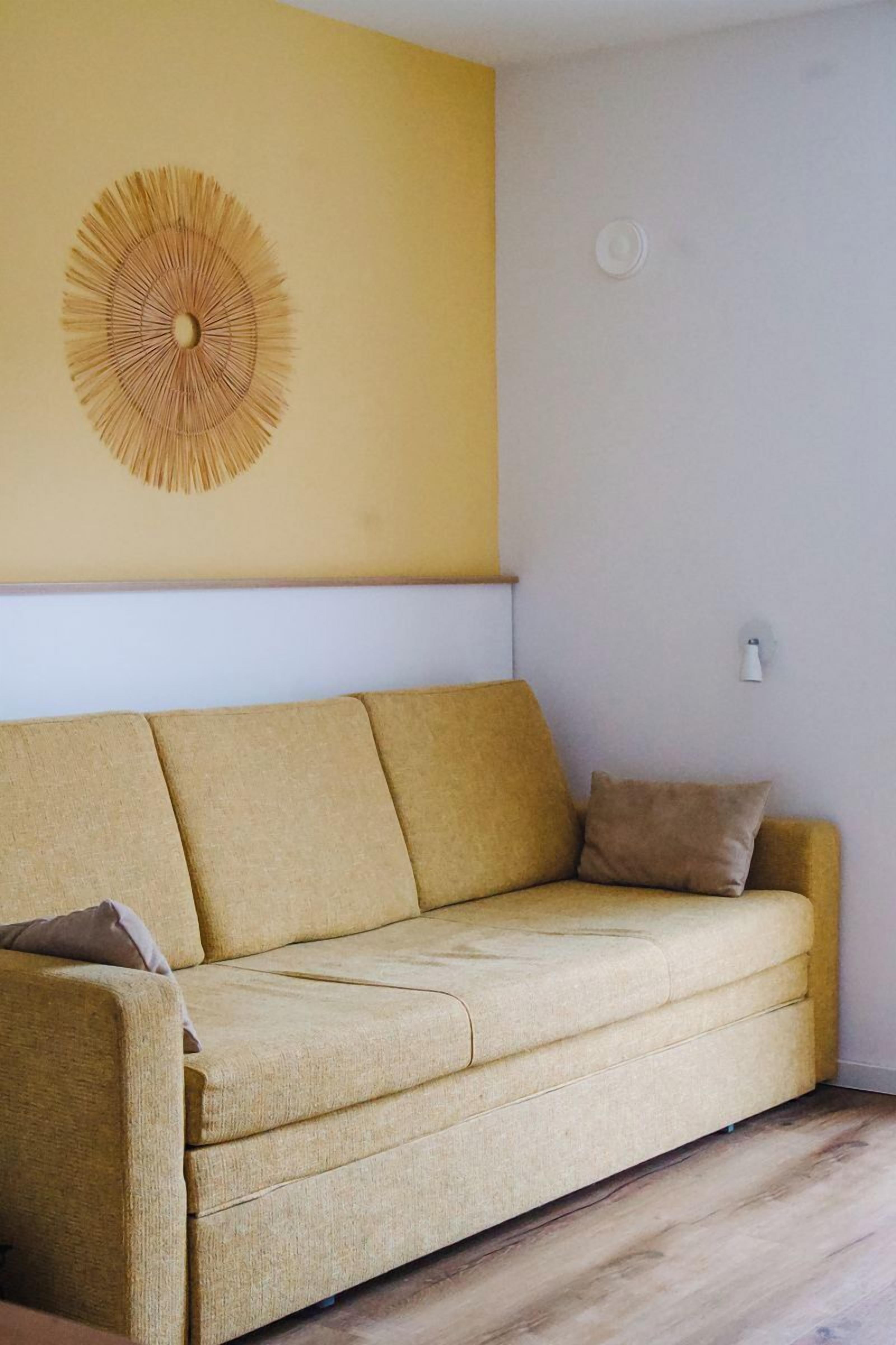 Ein gelbes Sofa mit Kissen, eine Wand mit einem Rundmuster und ein Lichtschalter.