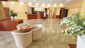 Un vestíbulo de hotel con mostrador de recepción, una zona de espera con asientos acolchados y una recepción.