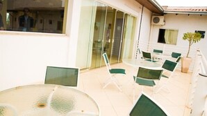 An outdoor patio with round tables and green chairs, a glass door leading inside, and a potted plant. - Druds Hotel (Tres Lagoas)
