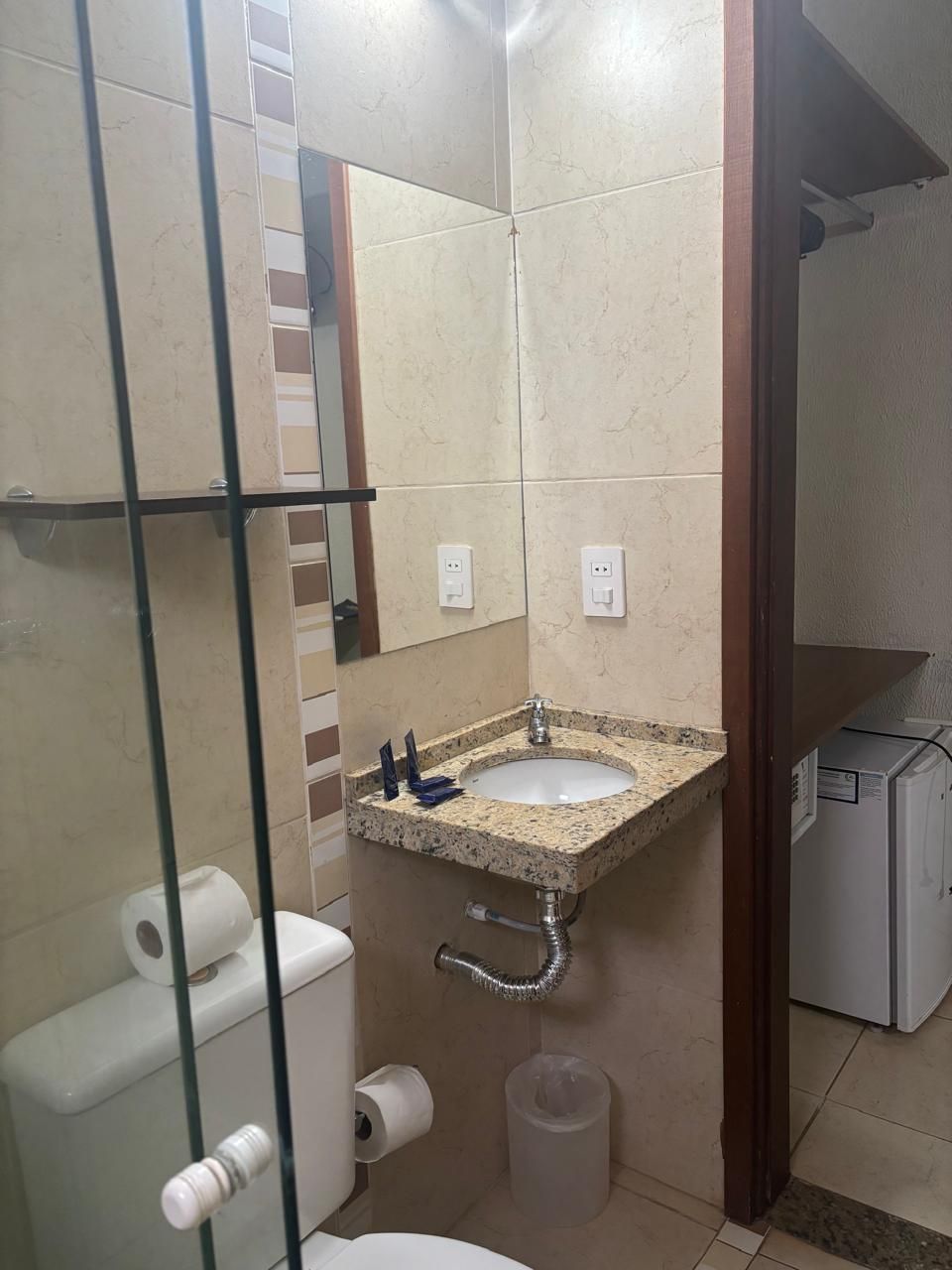 A bathroom with a glass shower enclosure, a sink with a marble countertop, a toilet, and a small trash bin.