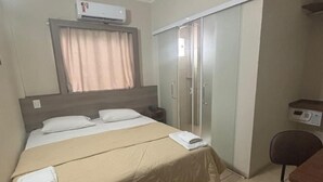 A hotel room with a bed, a desk, a wardrobe, and an air conditioning unit. - Druds Hotel (Tres Lagoas)