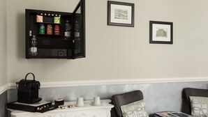 Une chambre dotée d’un mini-bar, de tableaux encadrés aux murs, d’une machine à café et de sièges agrémentés de coussins.
