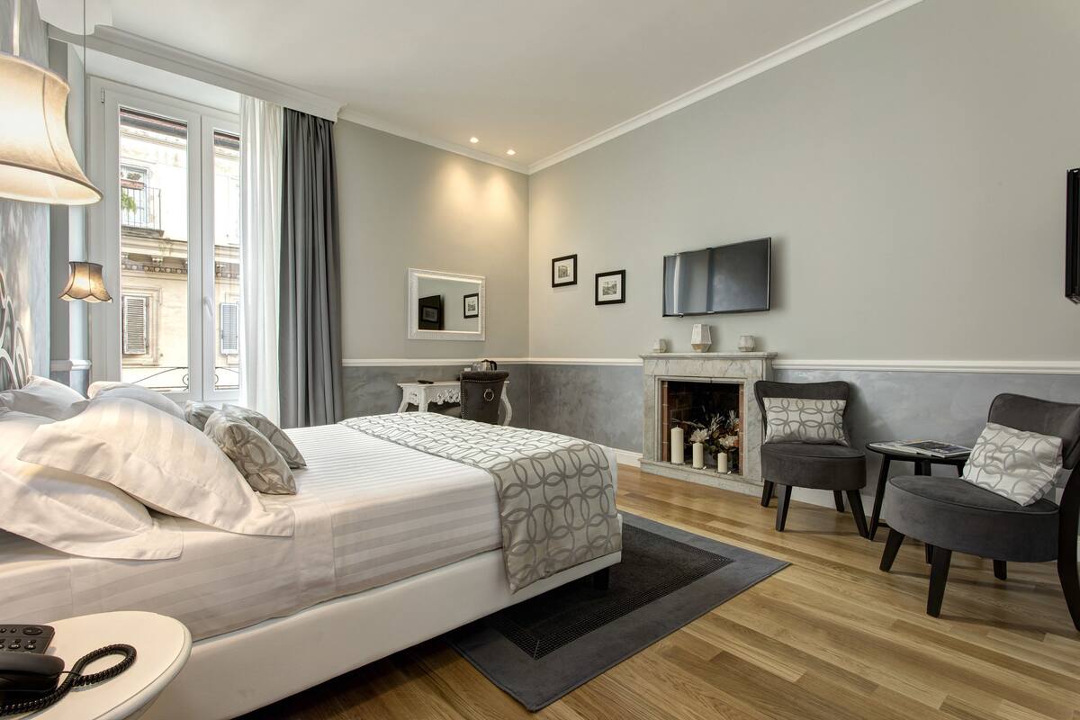 A modern hotel room with a large bed, a fireplace, a TV, and a view of the city.