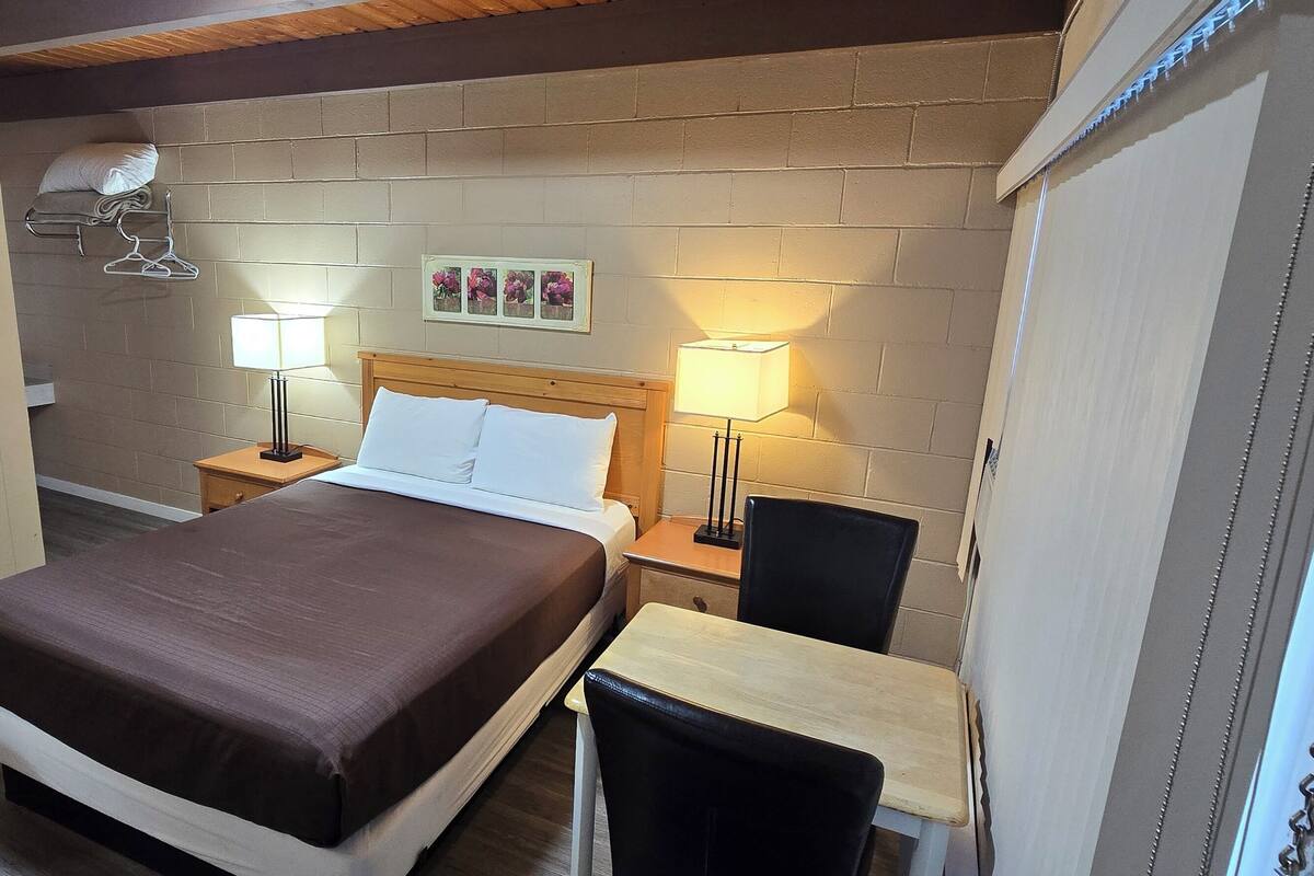 Una habitación de hotel con una cama, dos mesitas de noche con lámparas, una silla y un armario.