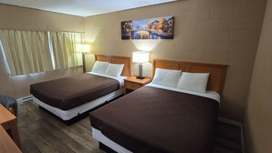 A hotel room with two beds, a wooden headboard, a painting on the wall, and a window with curtains. - Flamingo Motel (Penticton)