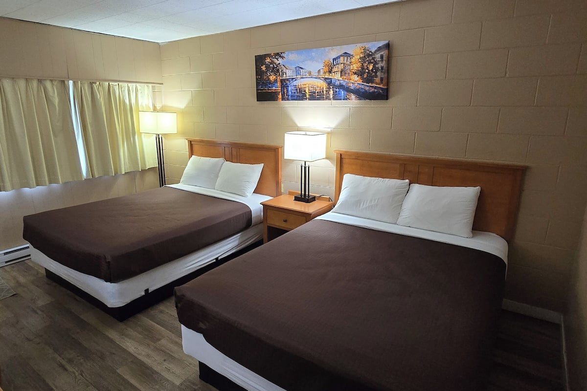 Habitación de hotel con dos camas, cabecero de madera, un cuadro en la pared y una ventana con cortinas.