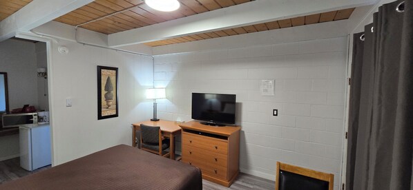 Une chambre comprenant un lit, un bureau, une chaise, une télévision et une petite kitchenette.