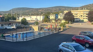 A parking lot with a swimming pool, a motel sign, and a mountain in the background. - Flamingo Motel (Penticton)