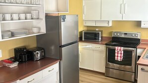 A compact kitchen with white cabinets, a stainless steel refrigerator, a microwave, a toaster, and an oven. - Flamingo Motel (Penticton)