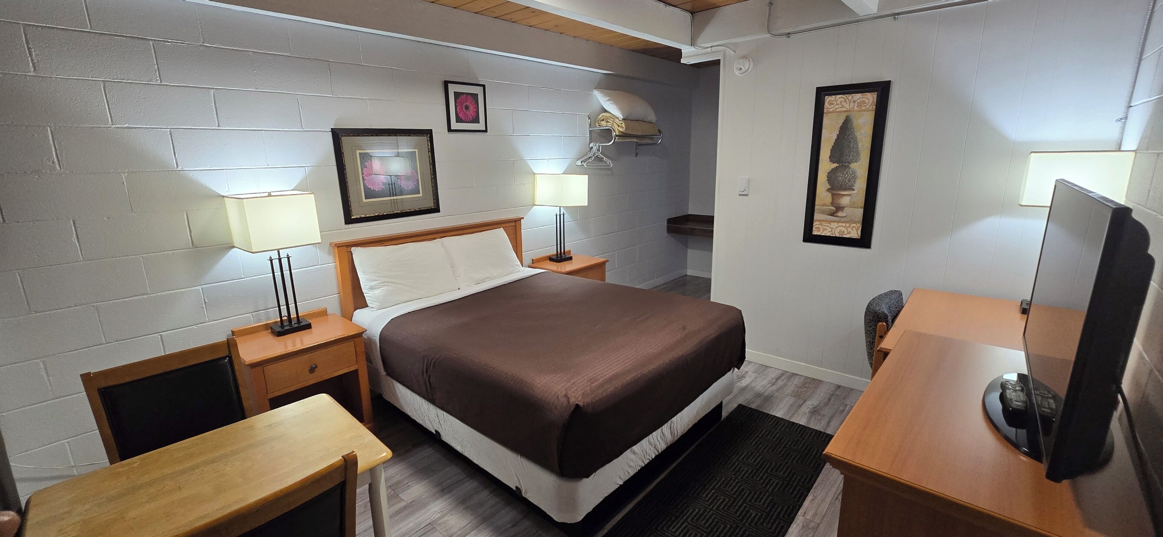 A hotel room with a bed, bedside tables, lamps, a desk, and a television.