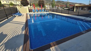 A rectangular swimming pool with a 3ft depth marker, surrounded by a black metal fence, and blue lounge chairs along the poolside. - Flamingo Motel (Penticton)