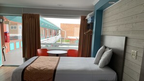 Una camera d'hotel con un letto grande, un comodino, un tavolino rotondo con due sedie e vista su un edificio e un ponte.
