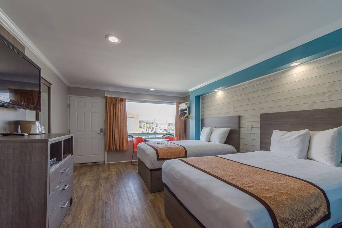 A hotel room with two beds, a dresser, a mirror, and a window with curtains.
