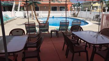 Zona junto a la piscina con sillas y mesas bajo un toldo rojo, con vistas a una piscina.