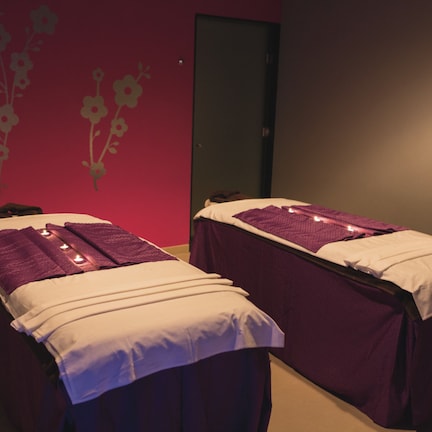 Two massage tables with white and purple linens, a red wall with floral decals, and a closed door.