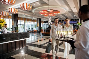 A hotel lobby with a reception desk, modern decor, and a waiter carrying a tray of glasses.