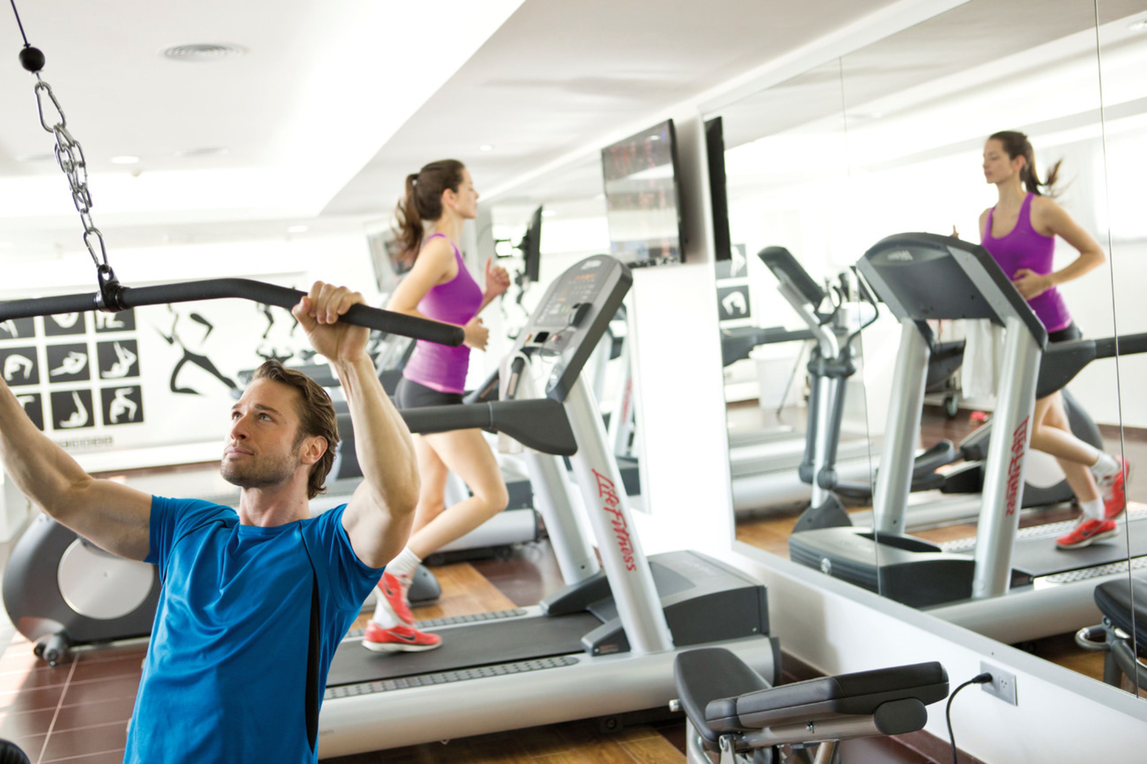 A gym with treadmills, a man lifting weights, and a woman running on a treadmill.