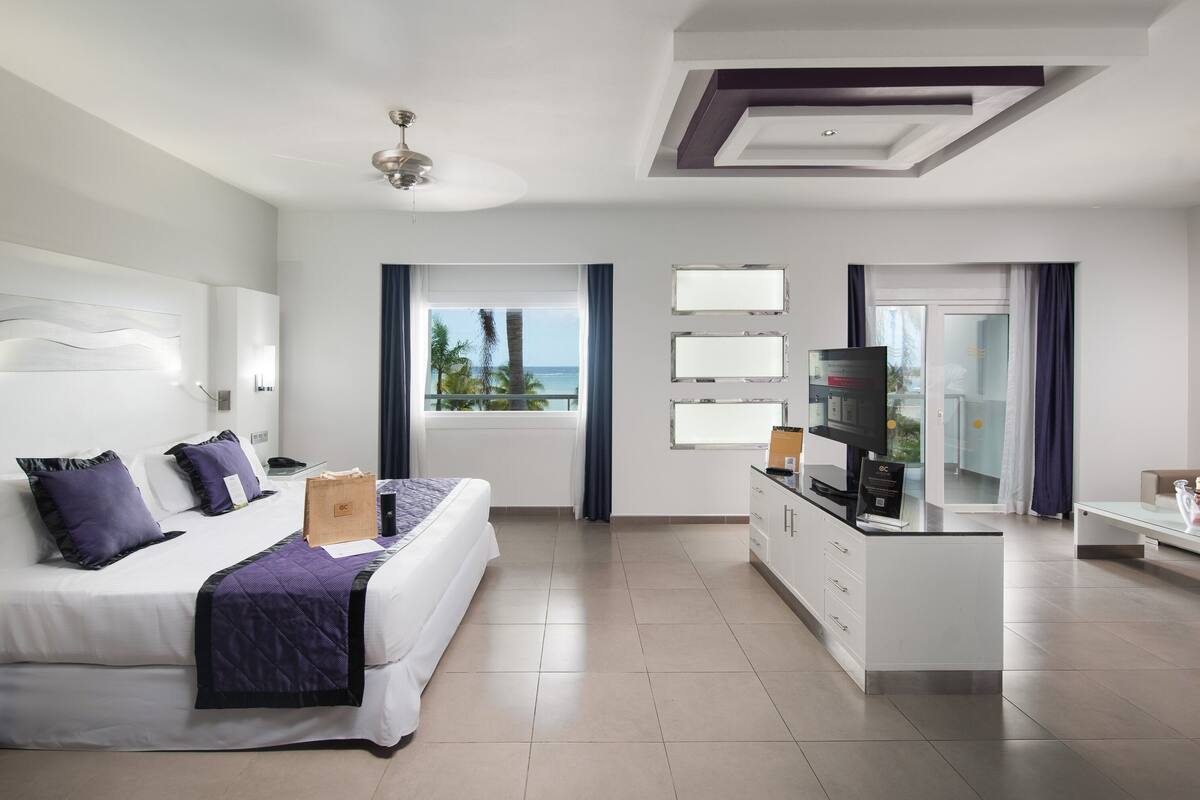A modern hotel room with a bed, a desk, a sofa, and a view of the ocean.