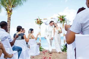 A beach wedding ceremony with white chairs and floral decorations.