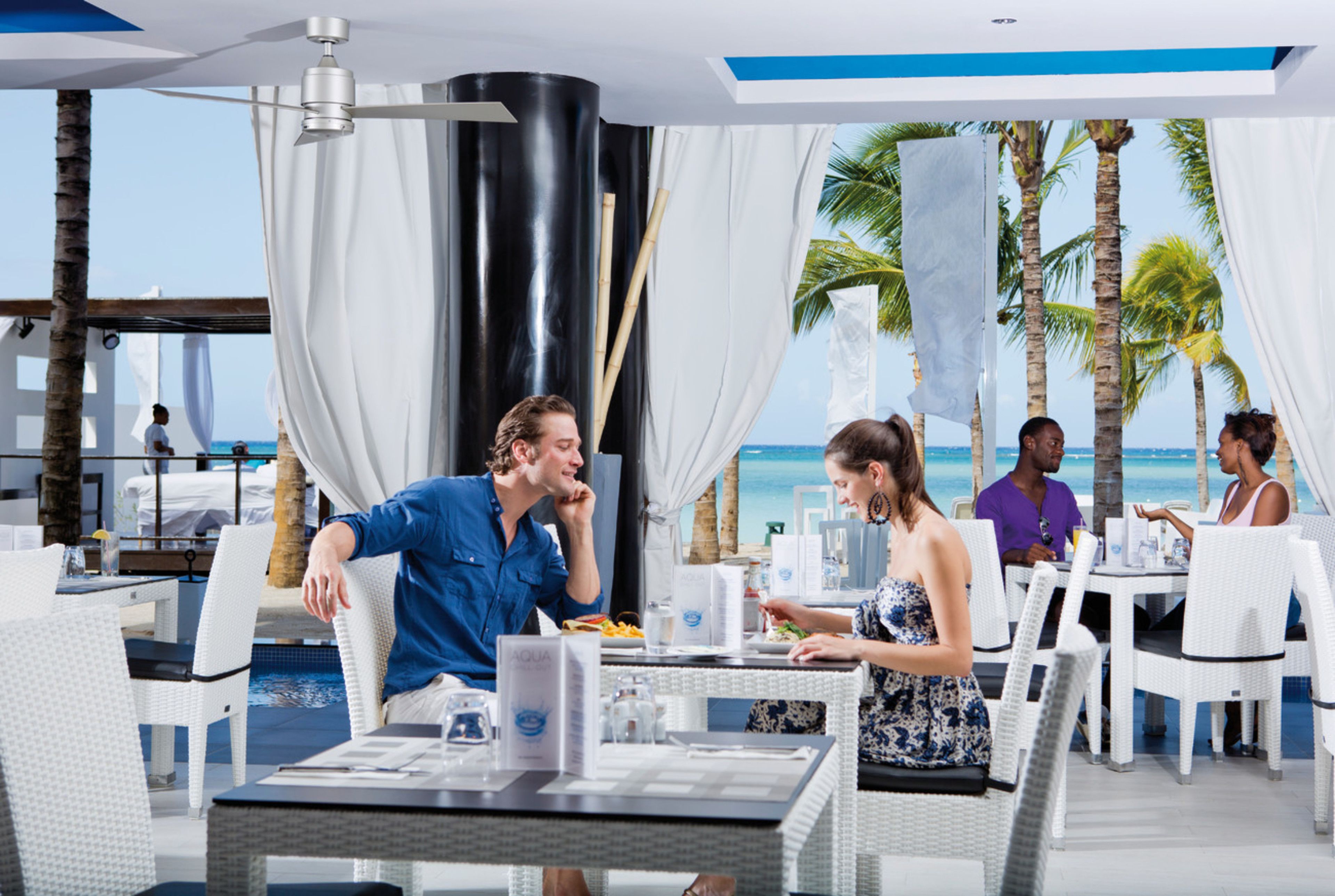A restaurant with white wicker furniture, a pool, and a view of the ocean.