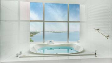 Un baño moderno con una bañera grande, vistas a un lago y una ventana con vista al cielo.