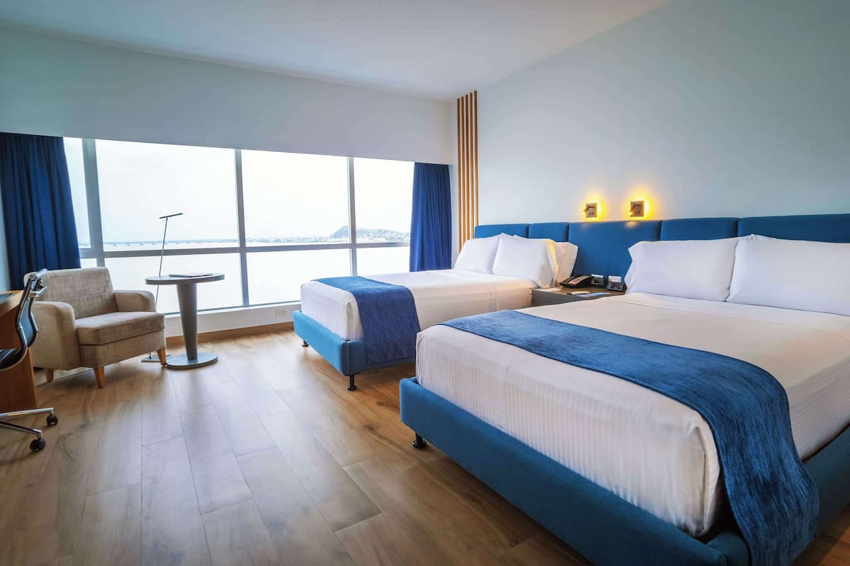 Habitación de hotel con dos camas, un escritorio, una silla y un ventanal que ofrece vistas.