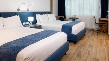 A hotel room with two beds, a desk, a chair, and a small table.