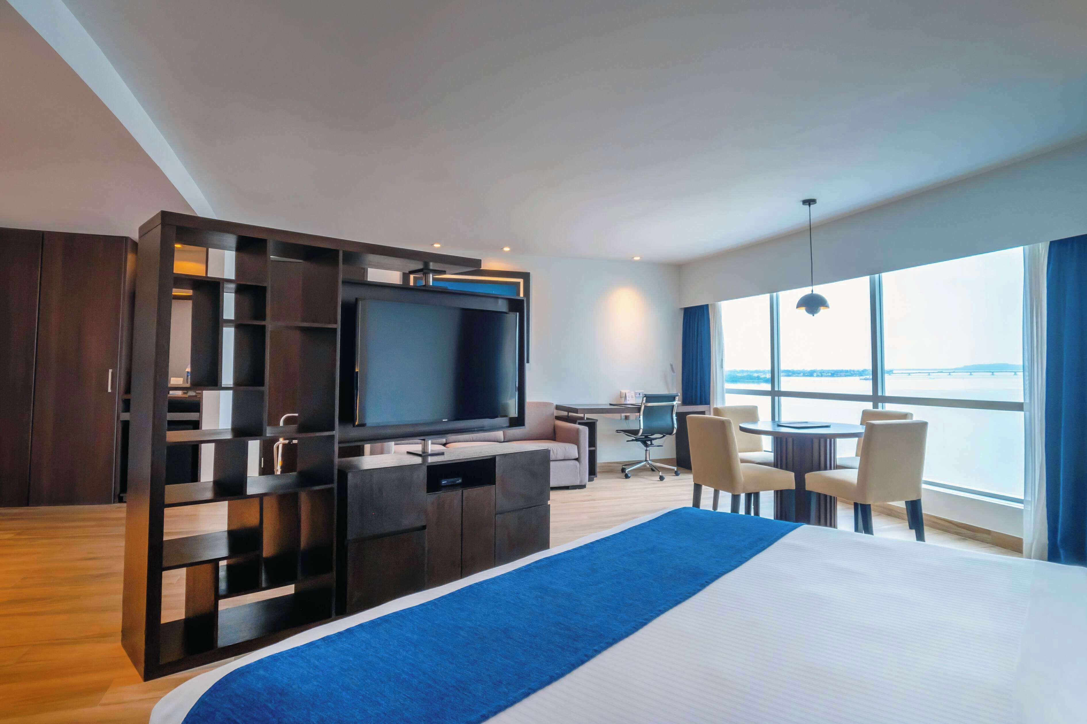 Habitación de hotel moderna con una cama grande, televisor de pantalla plana, escritorio con silla y vista al agua.