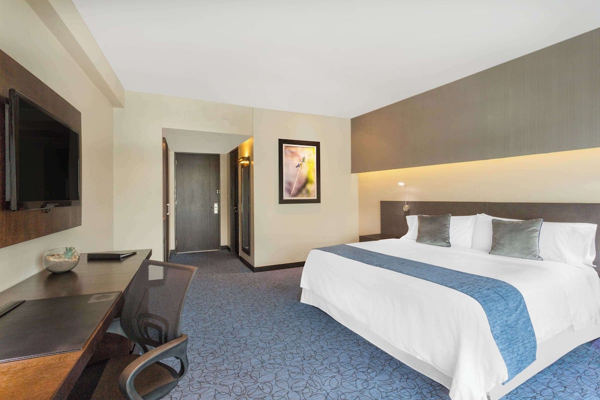 Una habitación de hotel con una cama grande, un escritorio con silla, un televisor de pantalla plana y una puerta que da a otra habitación.