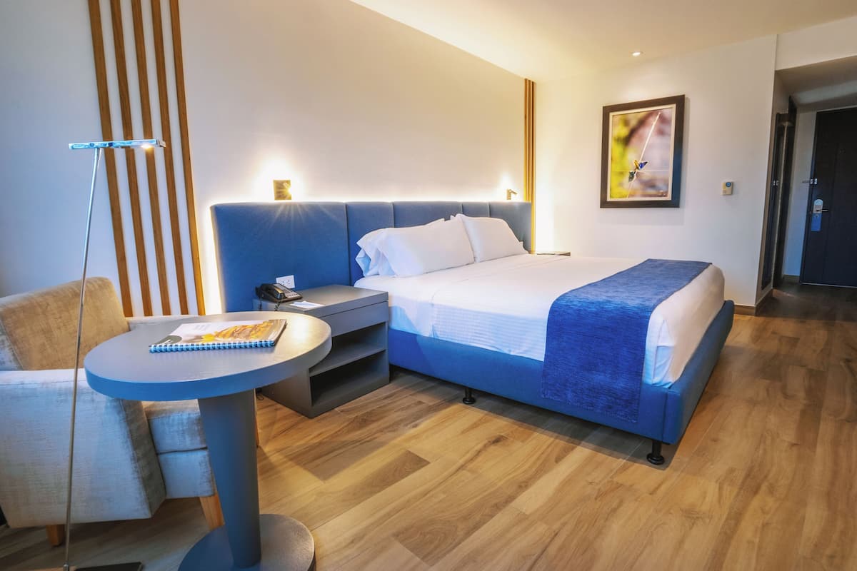 Una habitación de hotel moderna con una cama grande, una mesita de noche y una pequeña mesa redonda con un cuaderno.