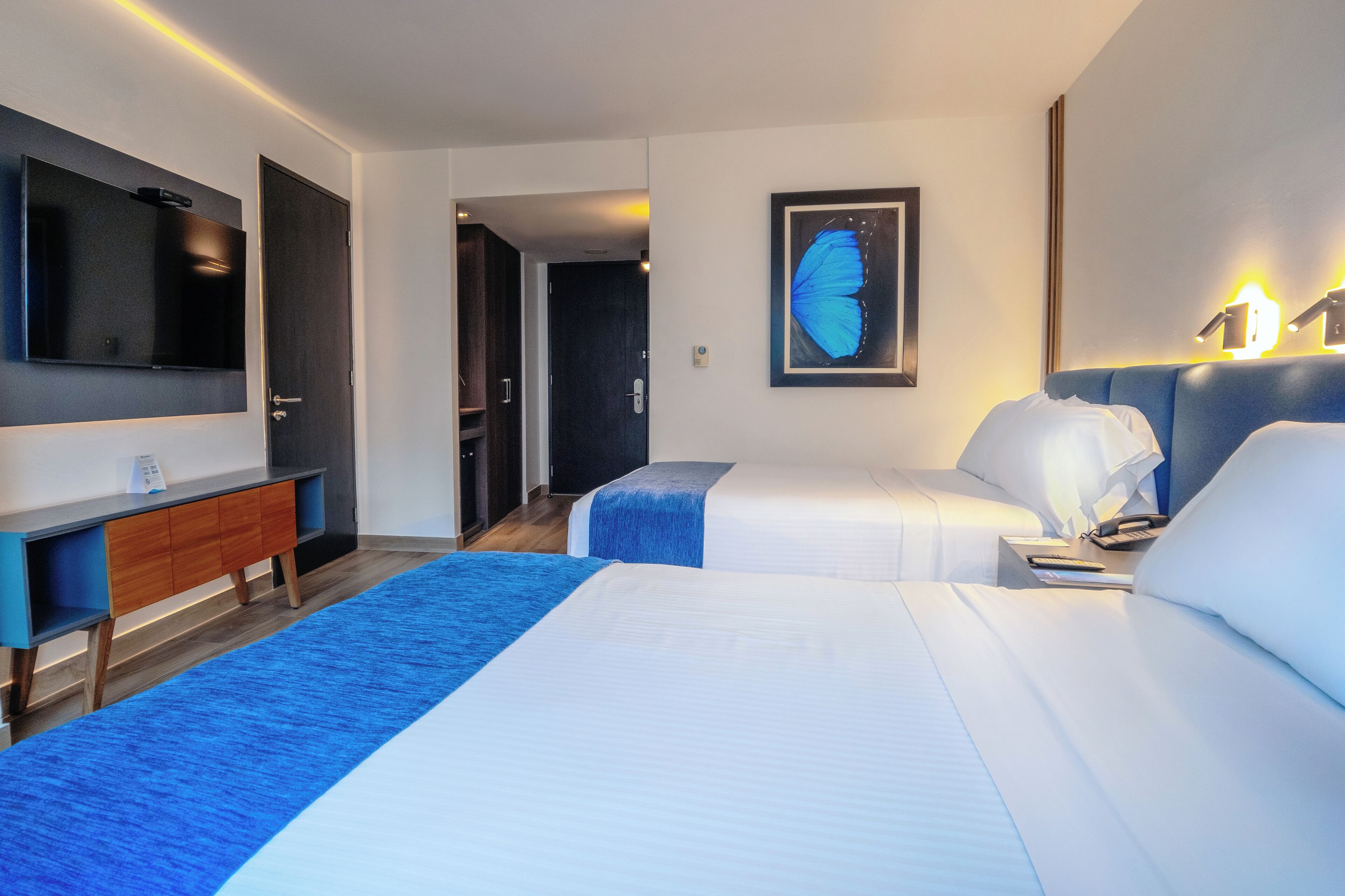 A hotel room with two beds, a TV, a desk, and a framed butterfly picture.