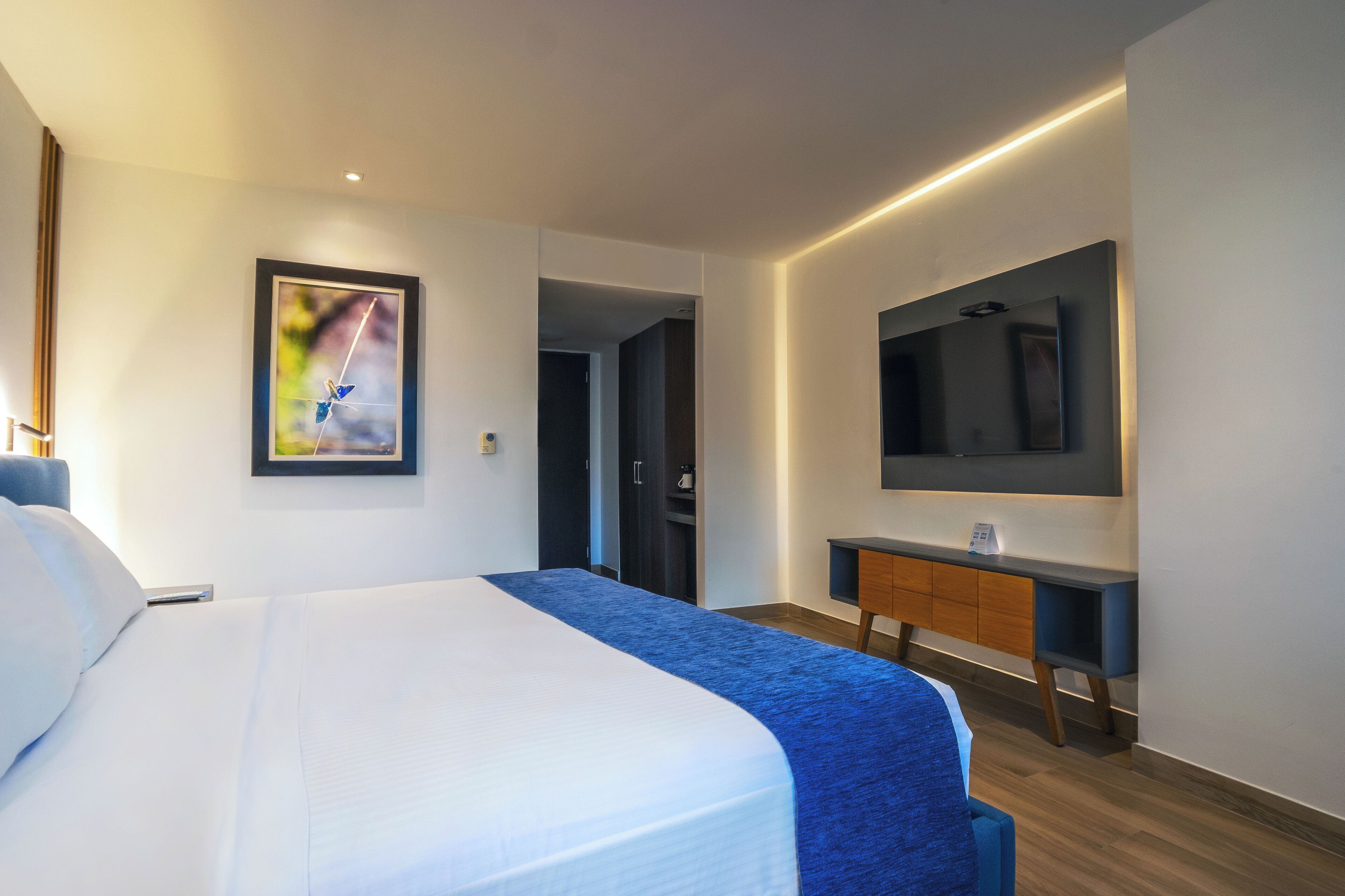 A modern hotel room with a large bed, a flat-screen TV mounted on the wall, and a small desk with a telephone.