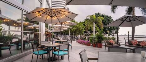 An outdoor dining area with tables and chairs, umbrellas, and potted plants.