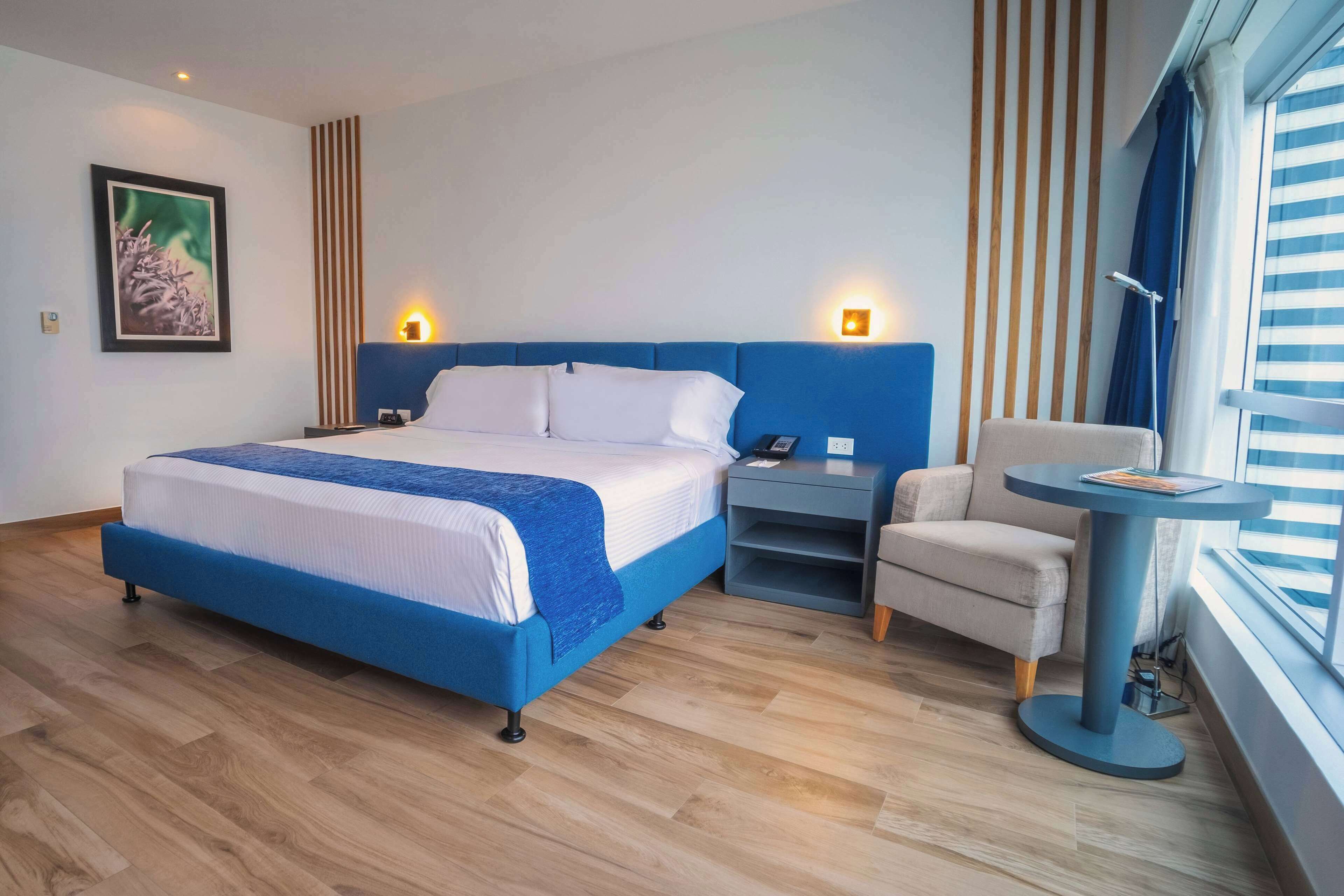 Habitación de hotel moderna con una cama grande, un escritorio, una silla y una ventana con persianas.