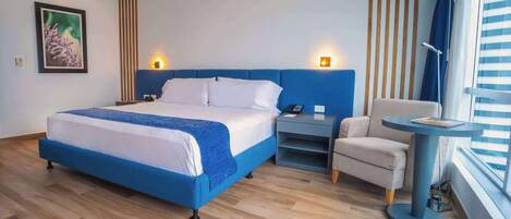 Habitación de hotel moderna con una cama grande, un escritorio, una silla y una ventana con persianas.