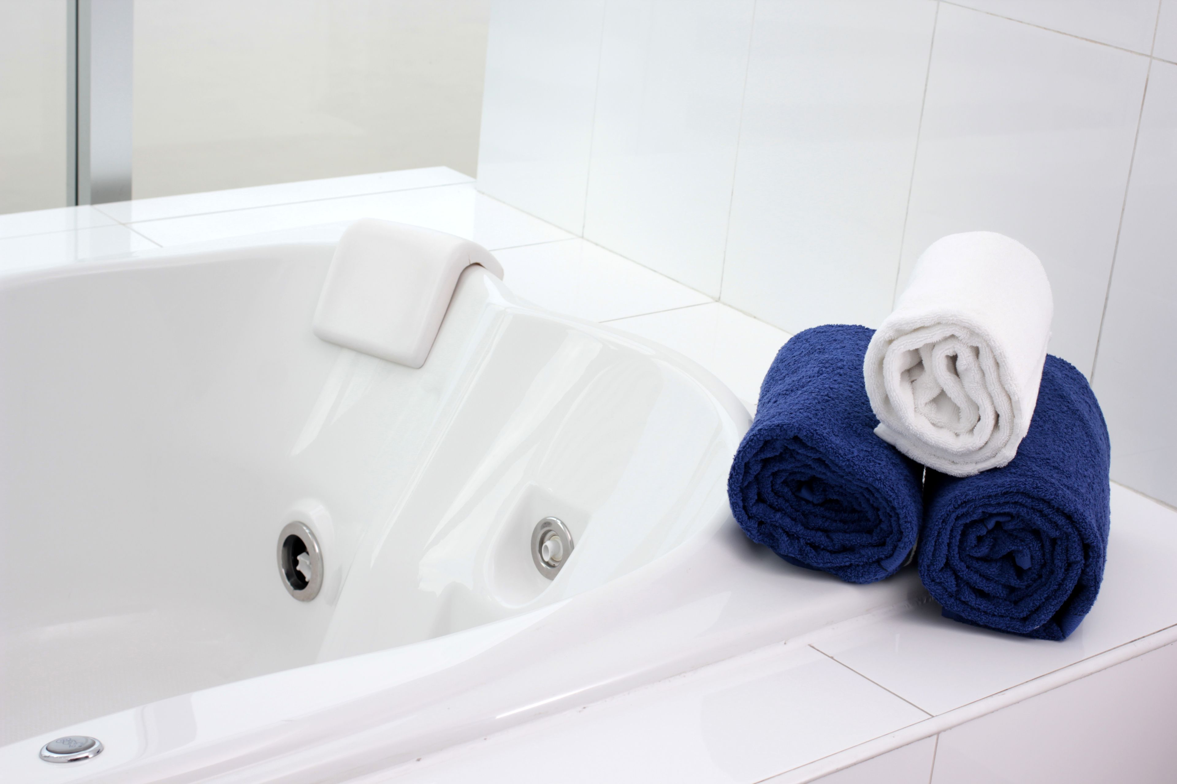 Una bañera blanca con una toalla blanca y dos toallas enrolladas.