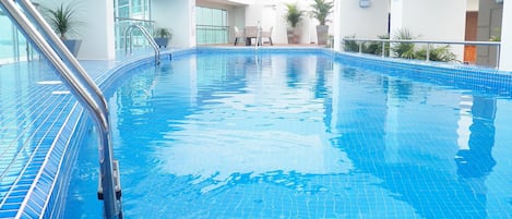 Una piscina interna con acqua cristallina e azzurra, circondata da pareti bianche e ampie finestre.