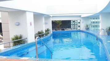 Una piscina interior con suelo de baldosas azules, barandillas de metal y vistas del interior del edificio.
