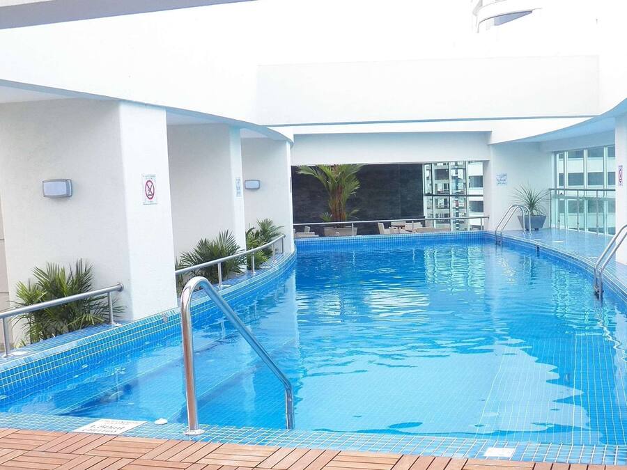 Una piscina interior con suelo de baldosas azules, barandillas de metal y vistas del interior del edificio.
