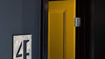 Una puerta con marco amarillo y puerta negra, un aparato de iluminación encima de la puerta, y una placa de metal con el número 4 en la pared.