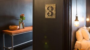 A room with a dark wall, a number '3' sign, a small table with a bowl and vase, and a bed with pillows. - The Franklin Hotel (Adelaide)