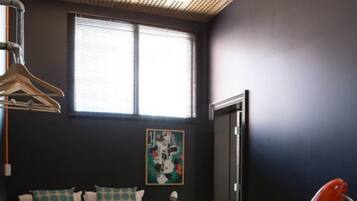 A bedroom with a bed, a bench, a desk with a lamp, a painting on the wall, and a window with blinds.