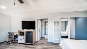 Ein modernes Hotelzimmer mit Holzboden, einem Bett, einem Schreibtisch mit Stuhl, einem Fernseher und einem Badezimmer mit Spiegel und Toilette.