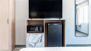 Ein Hotelzimmer mit Bett, Fernseher auf einem Holzregal, einer Mikrowelle und einem Kühlschrank.