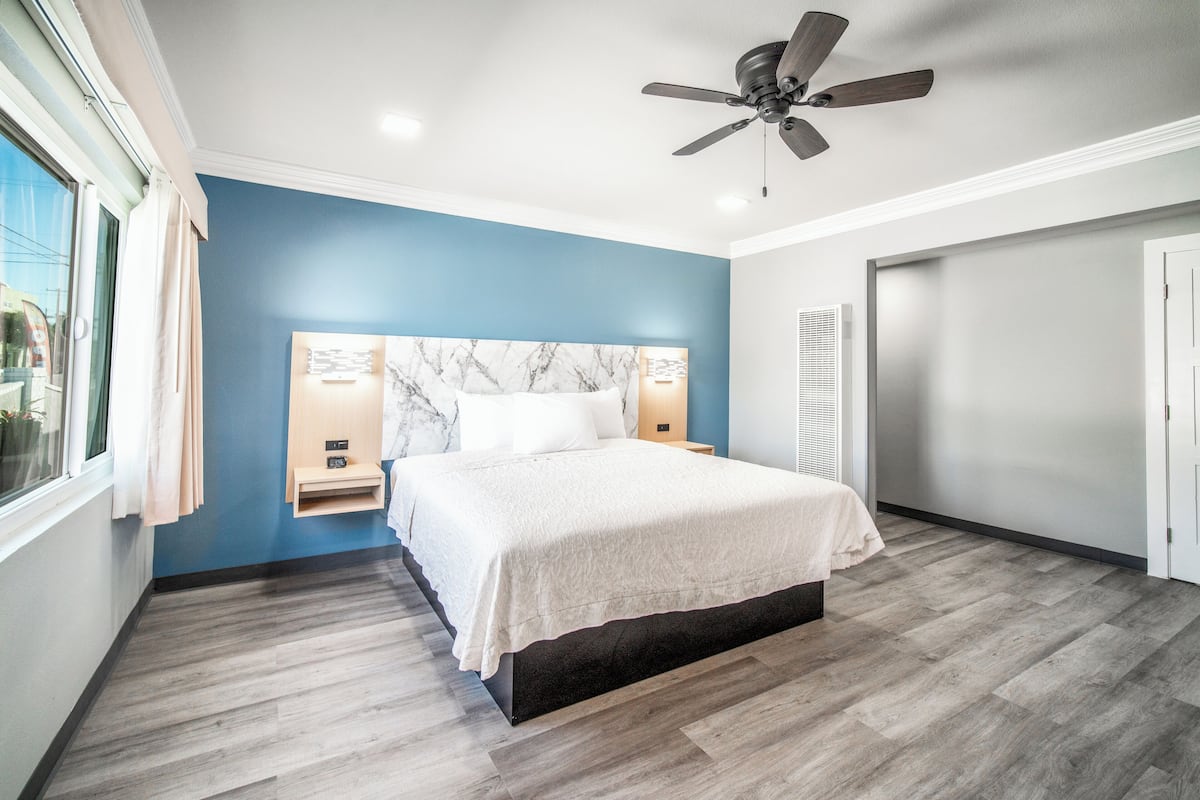 Un dormitorio con cama, ventilador de techo, cabecera de mármol y ventana con cortinas.