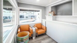 Ein Eckzimmer mit Fenster, einem kleinen Tisch, zwei orangefarbenen Stühlen und einem gestreiften Korb.