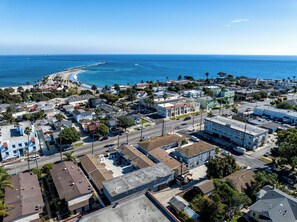 Vista aérea de un pueblo costero con edificios residenciales, un muelle que se adentra en el océano y un cielo azul despejado.