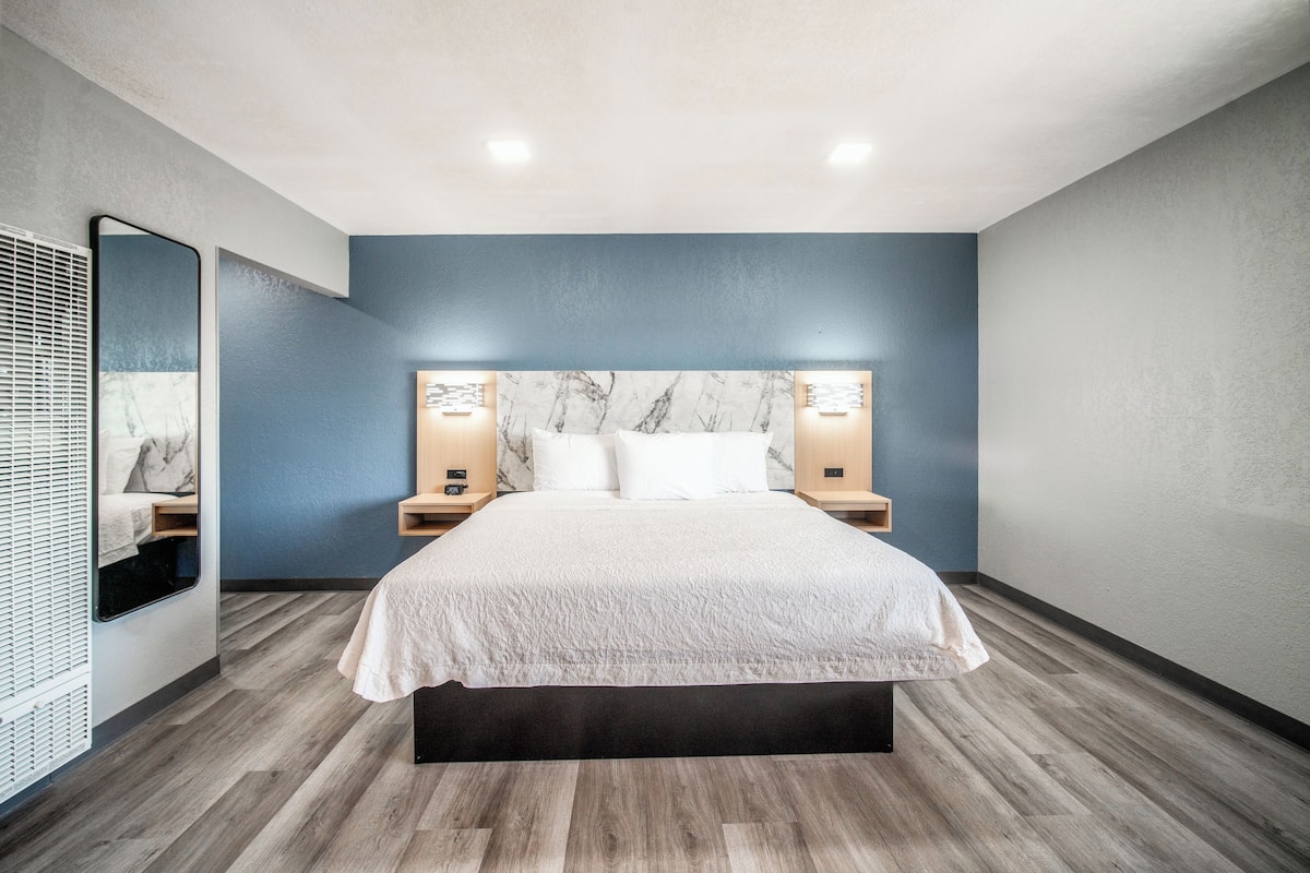 Un dormitorio moderno con una cama grande, piso de madera y una pared azul decorativa.