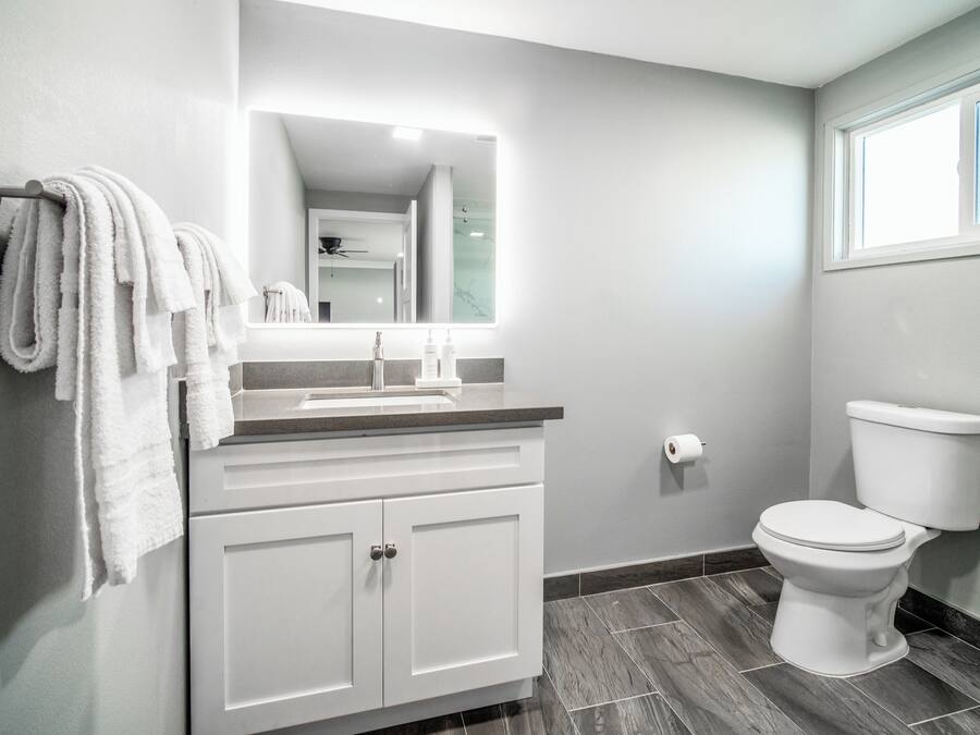 A bathroom with a white vanity, a mirror, a toilet, and a towel rack.